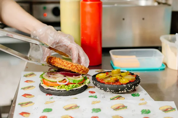 The process of making a chicken burger with fries in a black bun. The chef prepares a chicken burger with fries. Cooking burgers in the diner kitchen.