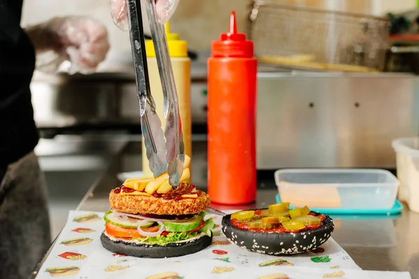 The process of making a chicken burger with fries in a black bun. The chef prepares a chicken burger with fries. Cooking burgers in the diner kitchen.