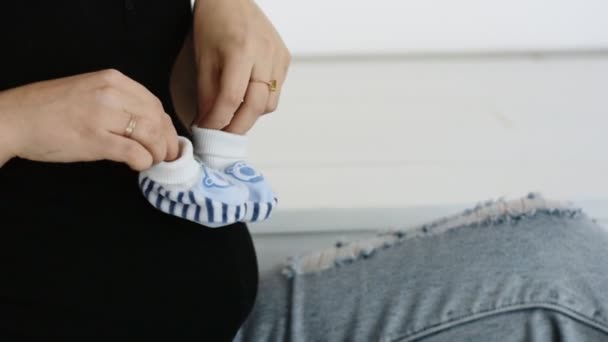 Junge schwangere Frau spielt mit Booties. Booties auf dem Bauch. Zeitlupe. Nahaufnahme — Stockvideo