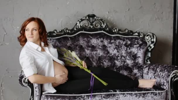 Hermosa mujer joven embarazada con el pelo rojo. En las manos sosteniendo un ramo de flores silvestres. .. Movimiento lento — Vídeos de Stock