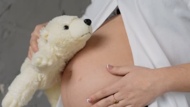 Happy pregnant woman in a white blouse. Keeps Teddy bears in his belly. The Teddy bear listens to the abdomen. — Stock Video