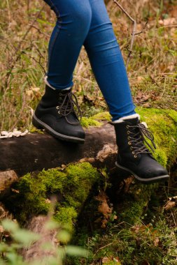 Sonbahar ormanında düşen ağaç gövdesinde siyah çizmelerle yürümek.