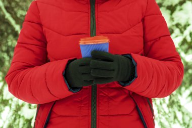 Kollar kahve ve kağıt bardak tutuyor. Karlı arka planda tek kullanımlık bir bardak tutan eller. Kış konseptine uygun kahve. Sıcak ve sıcak içecekler kış konseptinde.