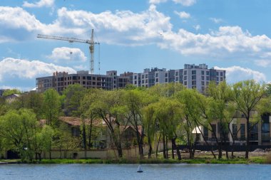 Kule vinçleri manzaralı bir nehir ve yeşil ağaçların yakınındaki yeni bir yerleşim yeri inşaatında çalışıyor..