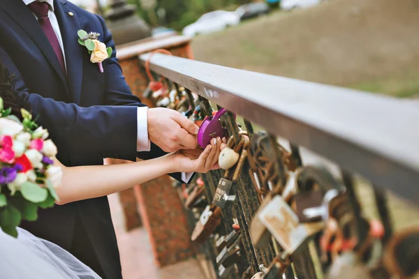 La serratura decorativa in mani di persone appena sposate, Spazio per testo su serratura. Bouquet da sposa sullo sfondo — Foto Stock