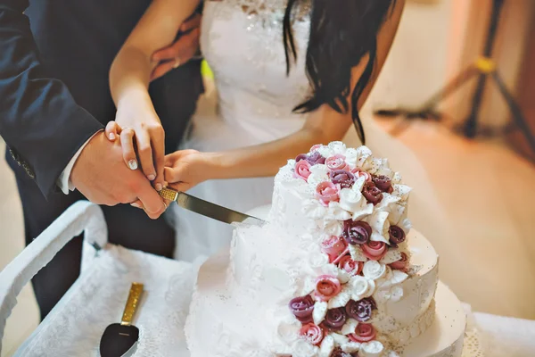 Eine Braut und ein Bräutigam schneiden ihre Hochzeitstorte mit lila und weißen Blumen an — Stockfoto