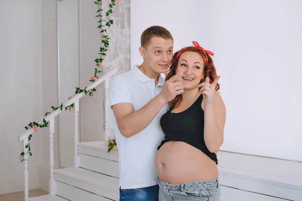 Heureux jeune homme et une jeune belle femme, regardant vers le côté. En prévision du bébé. Femme enceinte aux cheveux roux. Couple riant qui attend un bébé. Ventre nu enceinte . — Photo