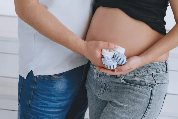 Mladý muž a mladá krásná žena na sebe dívali. V očekávání dítěte. Těhotná žena, zrzavý. Botičky na bříšku. — Stock fotografie