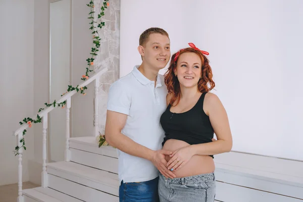 Heureux jeune homme et une jeune belle femme, regardant vers le côté. En prévision du bébé. Femme enceinte aux cheveux roux. Couple riant qui attend un bébé. Ventre nu enceinte . — Photo