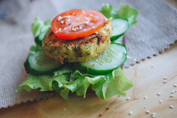 Vegan diyetinin Burger meze nohut mercimek pirzola, salatalık, taze marul ve domates ile. Susam serpin. Ahşap masa üzerinde sandviç.