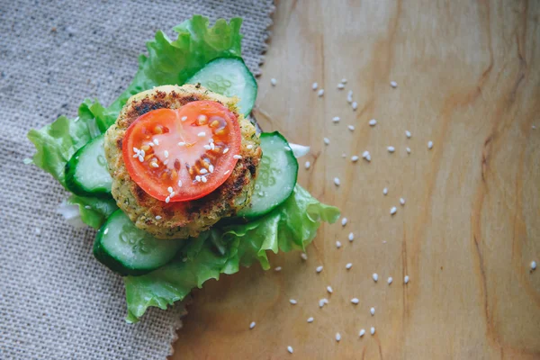 vegan diet Burger appetizer with chickpeas lentil cutlet, cucumber, fresh lettuce, and tomato. Sprinkle with sesame seeds. Sandwich on the wooden table.