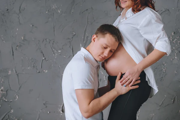 Člověk je všeobjímající břicho těhotné ženy. Zde je místo pro Tex. Na šedém pozadí. Dívá se na něj. — Stock fotografie