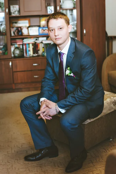 Portrait  young groom in a blue suit sitting on the couch — Stock Photo, Image
