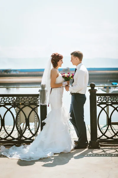 Sorrindo casal feliz no dia do casamento ponte, vestido branco noiva com trem, noivo em terno azul . — Fotografia de Stock