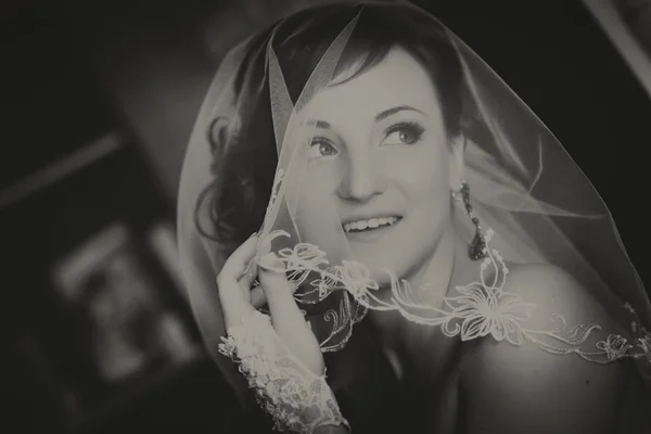 Portrait of young redheaded woman bride, through the wedding veil. Black and white photo.
