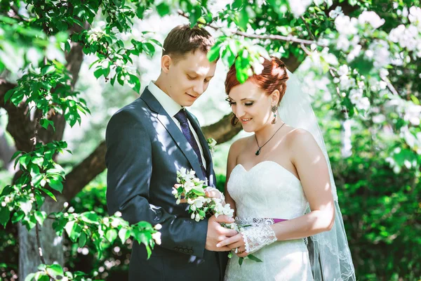 Heureux jeune mari et femme, dans les fleurs, ils regardent le bouquet . — Photo