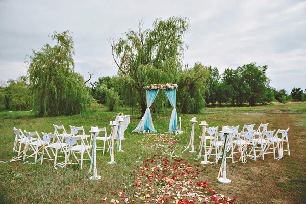 Um belo casamento. decoração do casamento no gramado, arco de casamento, cadeiras com fitas. turquesa, roxa e branca. As pétalas de rosa no chão. Cerimônia de casamento — Fotografia de Stock