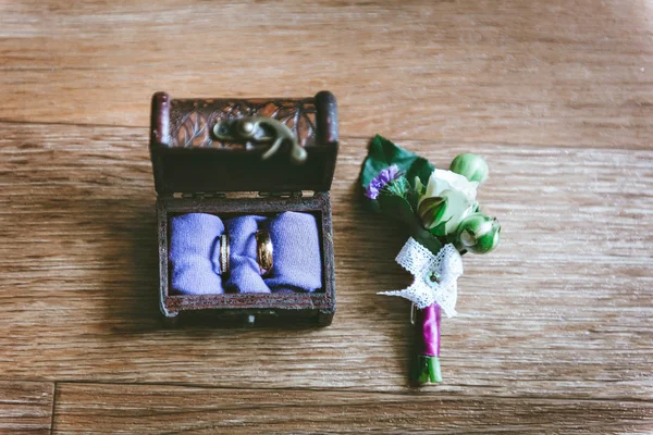 Wedding boutonniere. Gold rings lay in a wooden box. Purple white composition — Stock Photo, Image