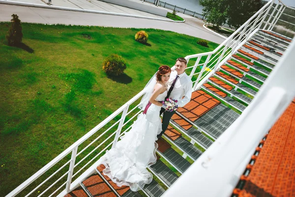 Portret van gelukkig liefdevolle paar staande in een omhelzing op trappen lacht, te chatten, te lachen. handen bruids boeket met wit, paars, roze bloemen. Uitzicht vanaf de top. Bruiloft jurk trein — Stockfoto