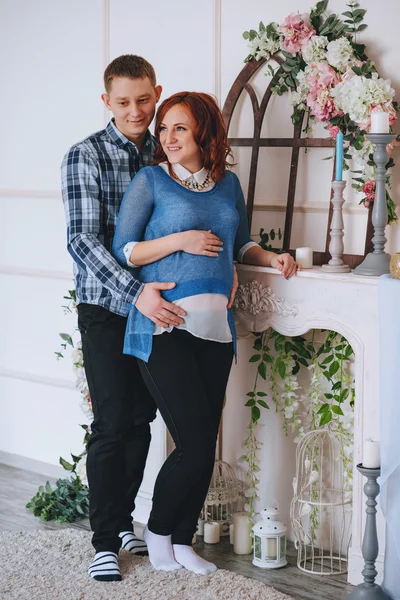 Těhotná mladý pár u krbu. Manžel obejme svou ženu. S barvami růženínu a nebesky modrá. — Stock fotografie