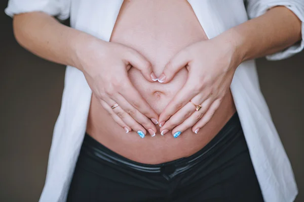 Die bauchschwangere Frau mit einem Herz aus Fingern. — Stockfoto