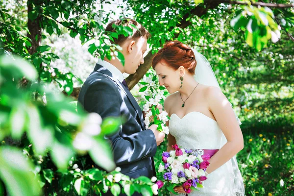 Heureux jeune mari et femme, dans les fleurs, ils regardent le bouquet . — Photo