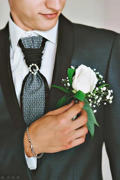 mens blue suit, red tie, white shirt. The groom adjusts his boutonniere of roses.