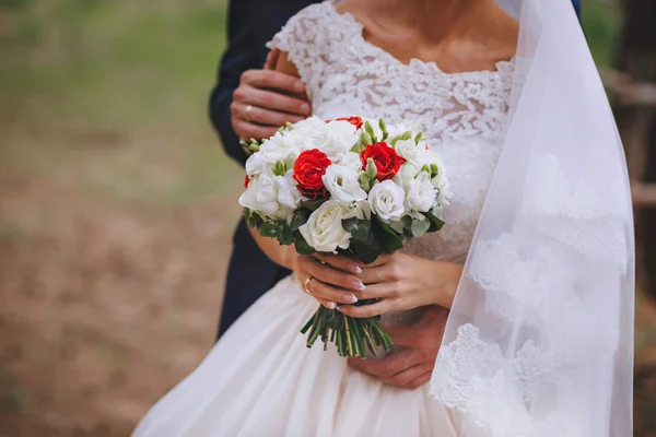 Buquê nupcial flores brancas vermelhas nas mãos dos recém-casados — Fotografia de Stock
