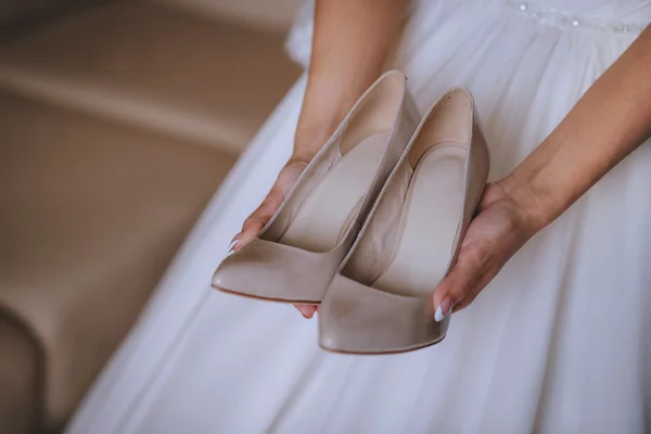 Zapatos beige clásico, en las manos de la chica, vestido blanco de fondo — Foto de Stock