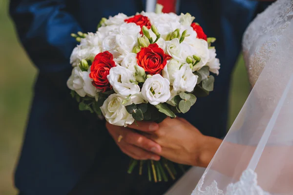 Buquê nupcial flores brancas vermelhas nas mãos dos recém-casados — Fotografia de Stock