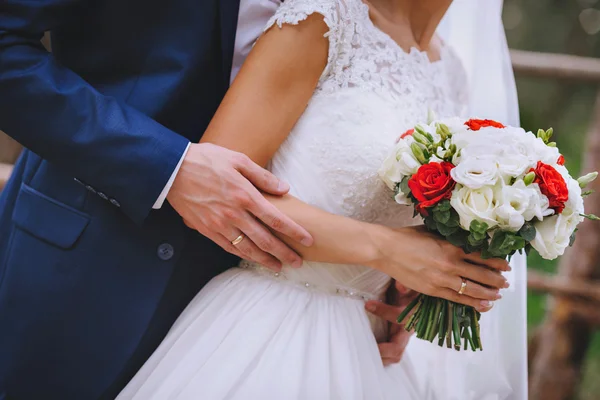 Bouquet de mariée fleurs blanches rouges dans les mains des jeunes mariés — Photo