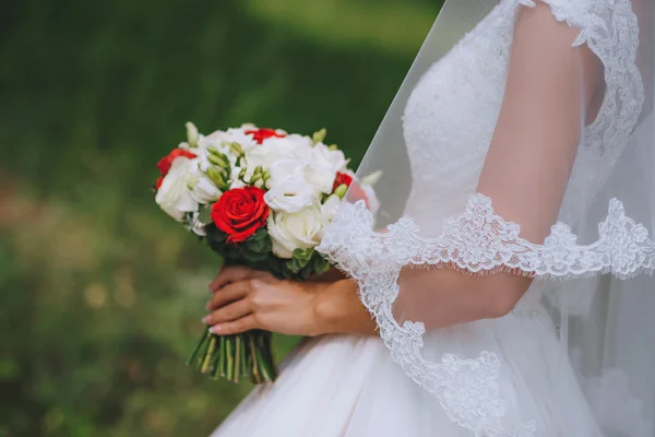 Brudbukett röda vita blommor i händerna på bruden — Stockfoto