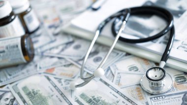 Steteskoplu reçeteli ilaç şişeleri ve uyuşturucu maliyetini, sigorta fiyatlandırma sorunlarını ve pahalı hasta tedavisini yansıtan Amerikan doları.