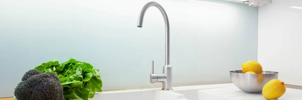 Panorama of simple, white kitchen sink with silver tap and glass backsplash