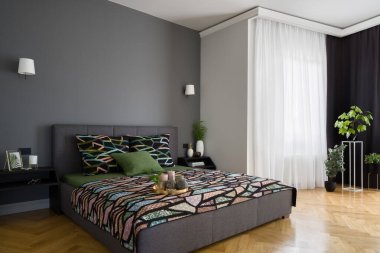 Büyük yataklı güzel yatak odası, modern gri duvar ve zarif ahşap zemin, uzun perdelerin arkasındaki pencere ve birçok şık dekorasyonla.