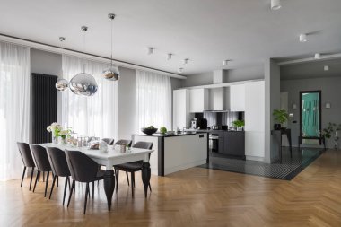 Süslü beyaz mutfak, uzun dekore edilmiş yemek masası gri sandalyeler ve şık ahşap zemin.