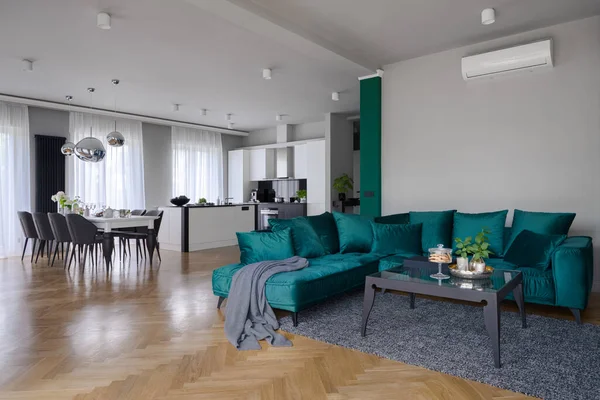 Spacious apartment with beautiful kitchen with dining table and elegant living room with stylish green corner sofa and modern coffee table