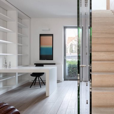 Beyaz rafları ve ahşap merdivenli koridorun yanındaki masası olan basit bir ofis.