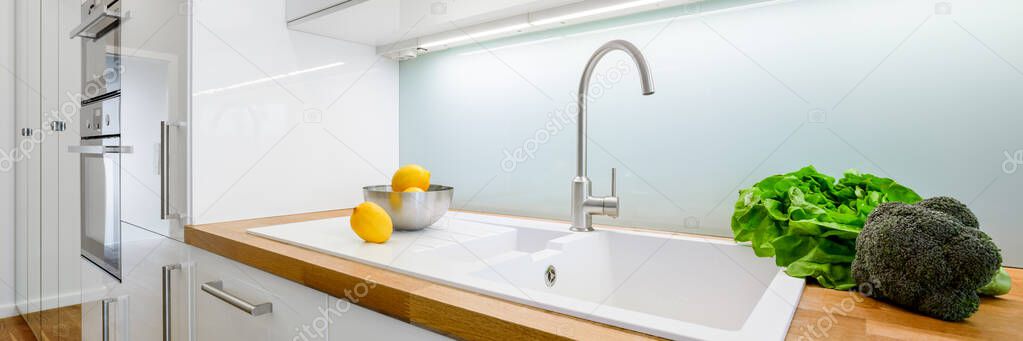Panorama of stylish white kitchen furniture with simple sink in wooden countertop