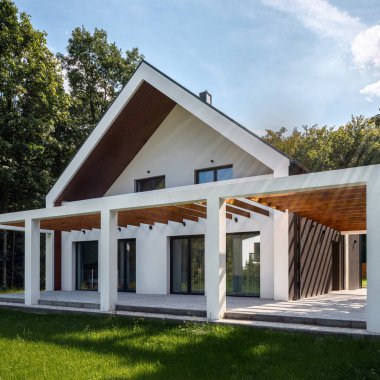 Modern, büyük teraslı ve yeşil bahçeli beyaz evin dış görünüşü. 