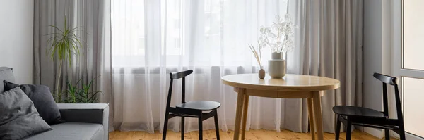 2つの黒のスタイリッシュな椅子と小さなリビングルームの装飾とシンプルな木製のダイニングテーブルのパノラマ — ストック写真