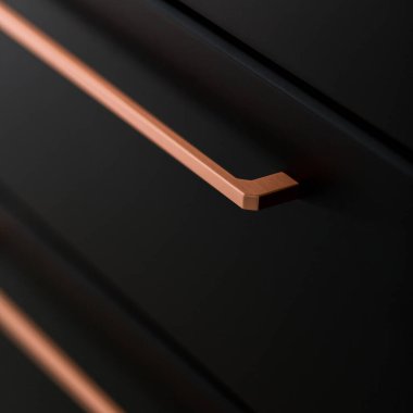 Modern siyah çekmecede şık bakır saplı yakın plan.