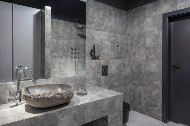Koyu ve modern banyo, gri duvar kiremitleri, lavabo gibi taş ve büyük ayna.