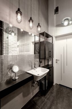 Gri ve siyah renkli, endüstriyel lambalı koyu ve şık bir banyo.