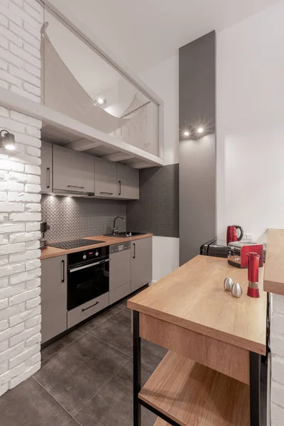 Simple and modern kitchen with gray furniture, white brick walls, gray floor tiles and wooden countertops