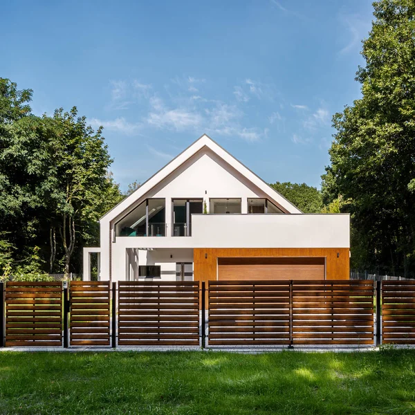 森の中のフェンスのような木の後ろのガレージと現代の白い家の外観 — ストック写真