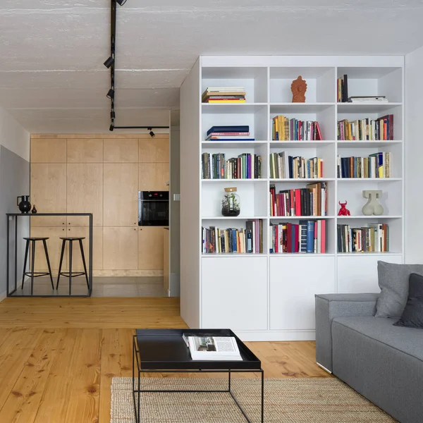 松の木の床と白い本棚の後ろのキッチンエリアとスタイリッシュなリビングルーム — ストック写真