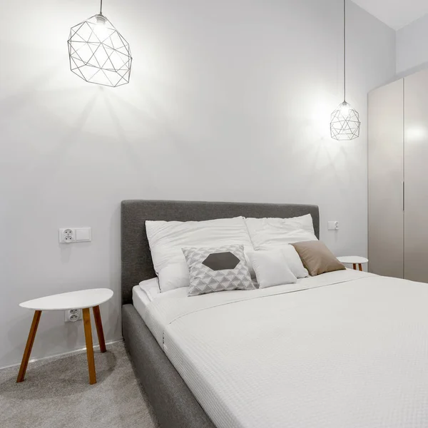 Simple bedroom with big bed, ceiling lights, modern bedside tables and gray carpet flooring