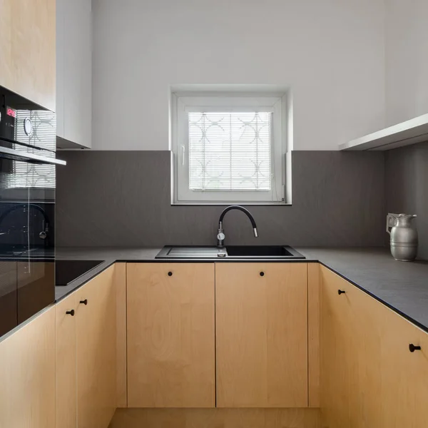 现代化厨房 橱柜上有桦木胶合板 深色的壁板台面 黑色的水池和水龙头 小的正方形窗户 — 图库照片