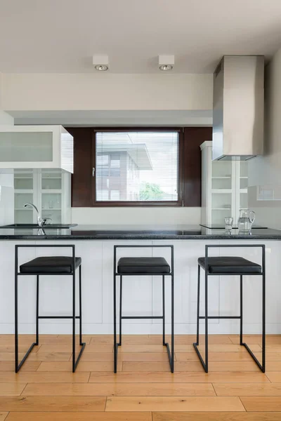 New kitchen with black countertop on kitchen island and three stylish, black bar stools